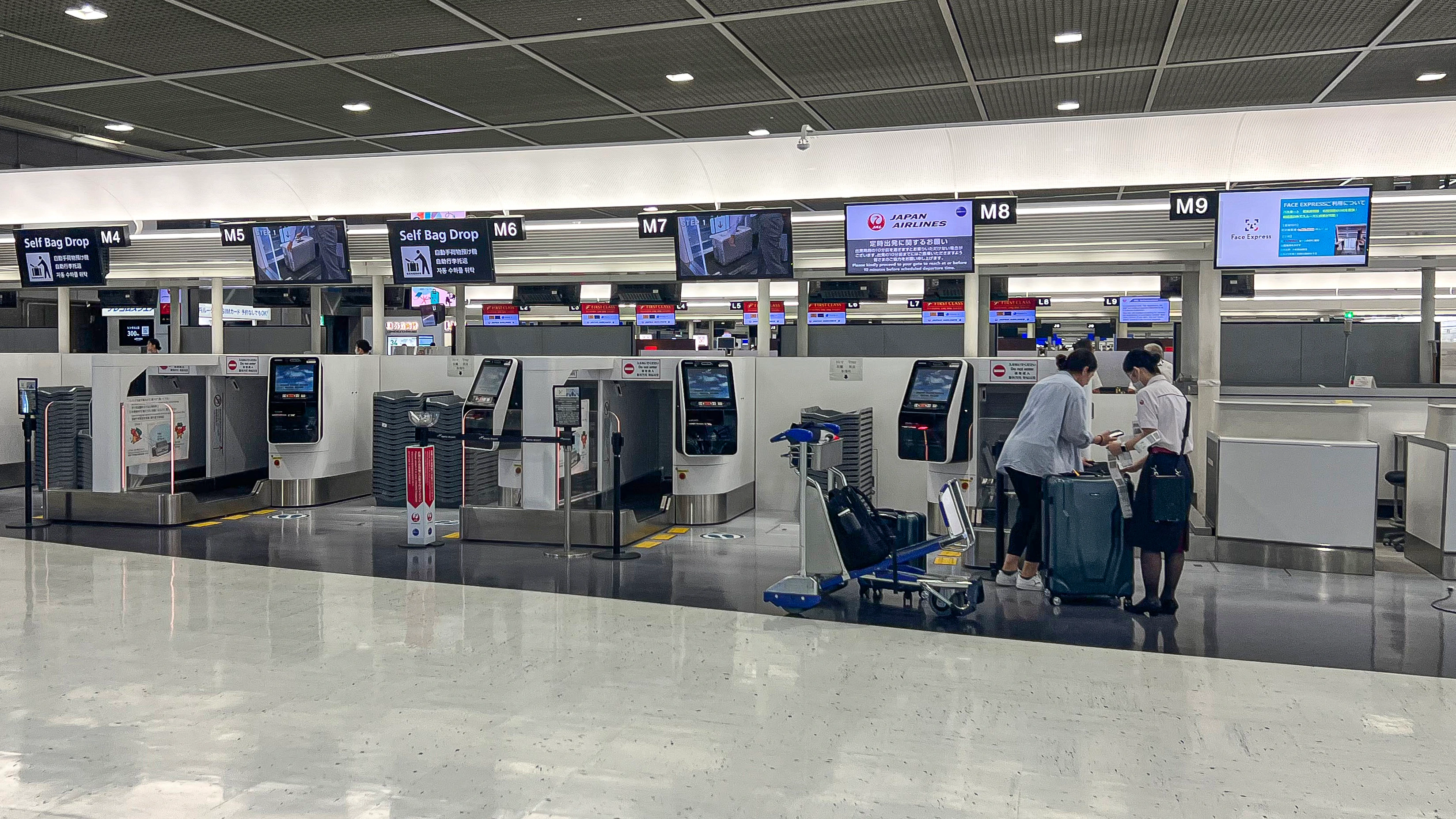 Archival JAL check-in and self bag-drop counters at Narita Terminal2, Japan, August2023, with two people beside luggage on the right.