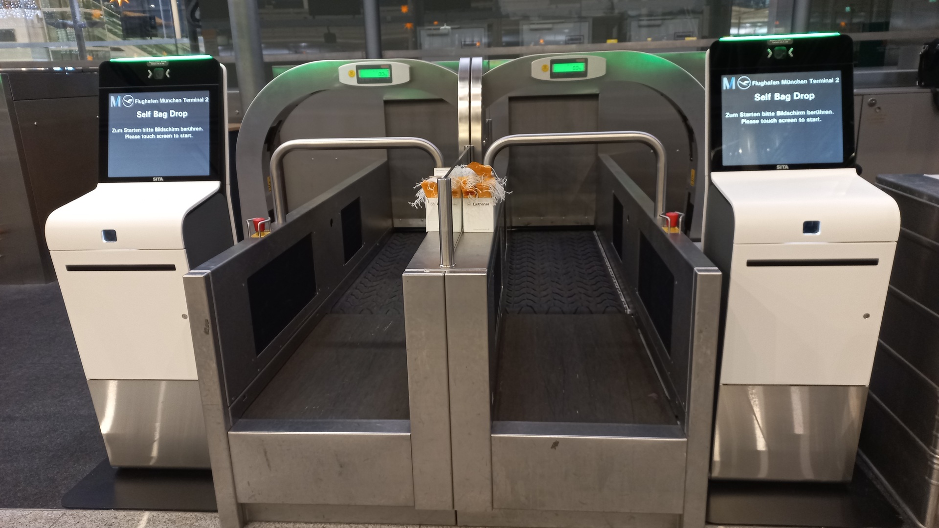 Two SITA-marked self-service bag-drop kiosks and conveyor lanes at Munich Airport Terminal 2 in November 2024.