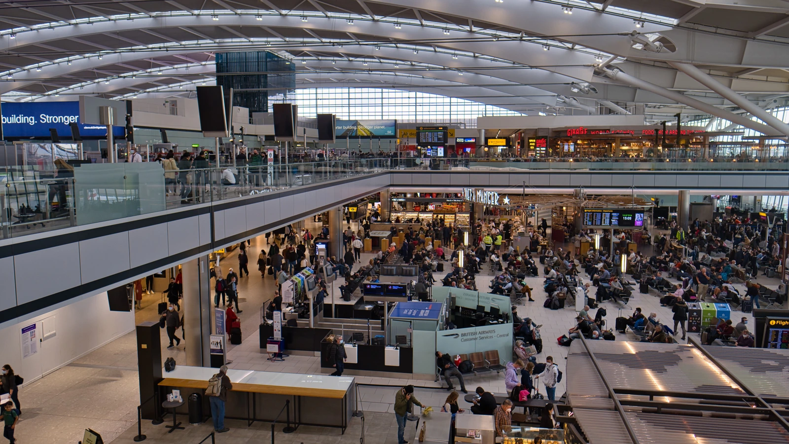 Archive photograph of passengers, seating and shops beneath the sweeping roof of Heathrow Terminal 5 in March 2022.